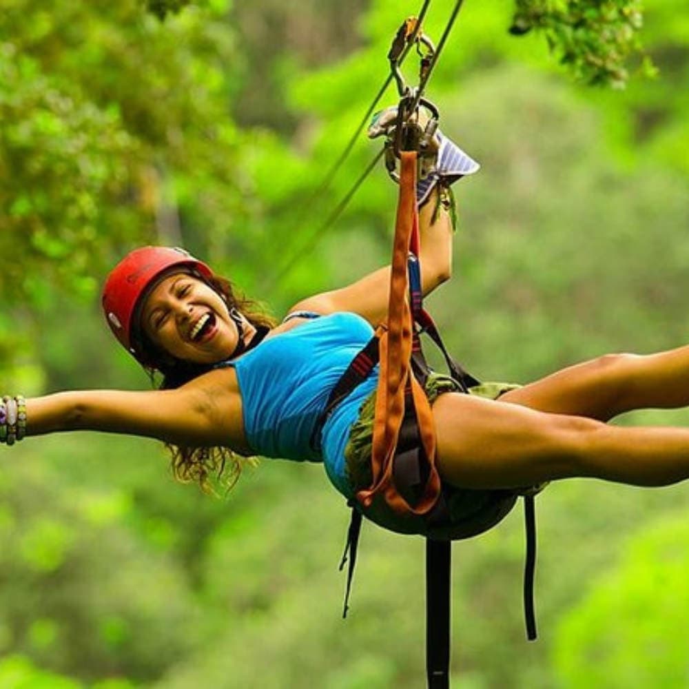 A person happily zip-lining through a lush green forest.