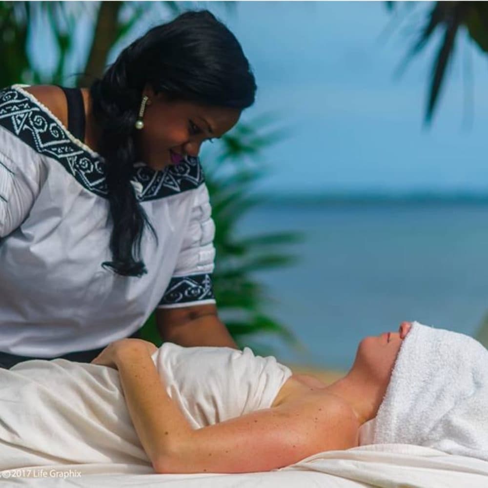 A massage therapist provides a treatment to a client on a beachside.