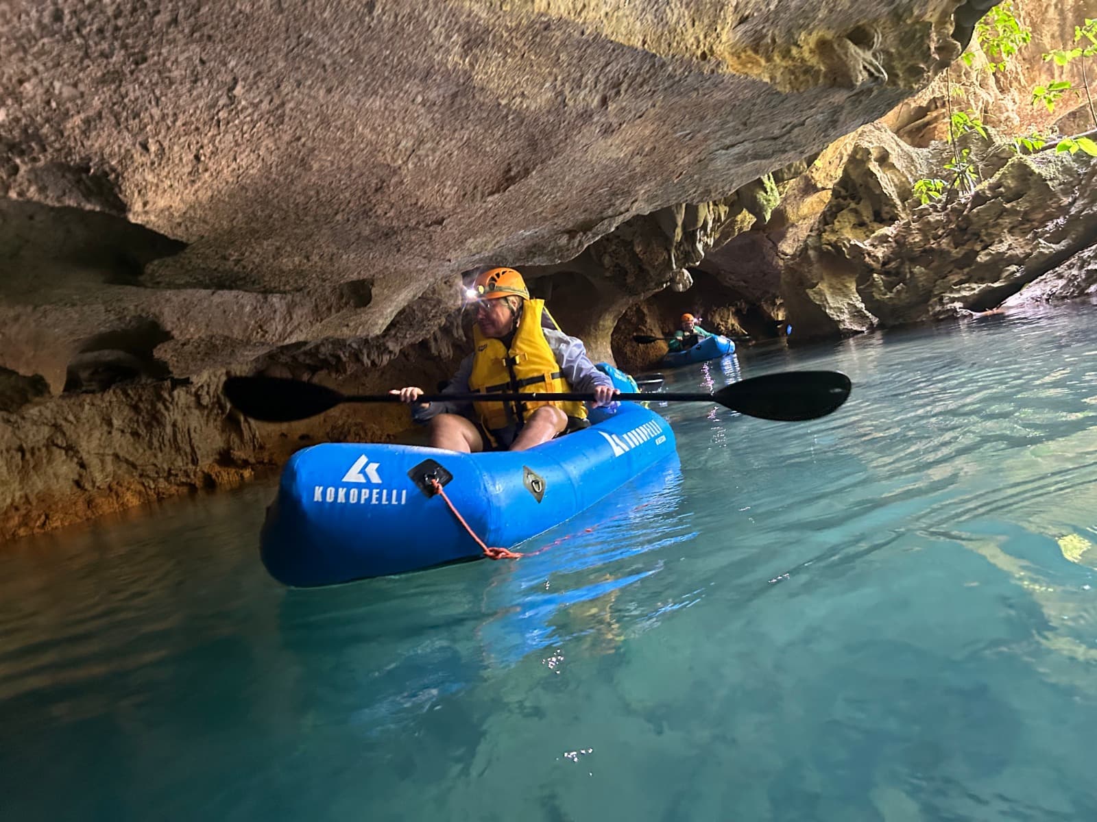 A person kayaks through a narrow cave with water reflecting the light above.