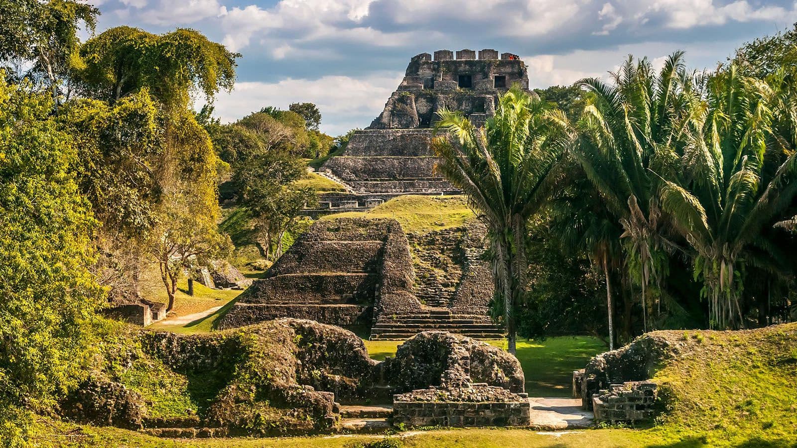 An ancient temple surrounded by lush greenery and palm trees under a cloudy sky.
